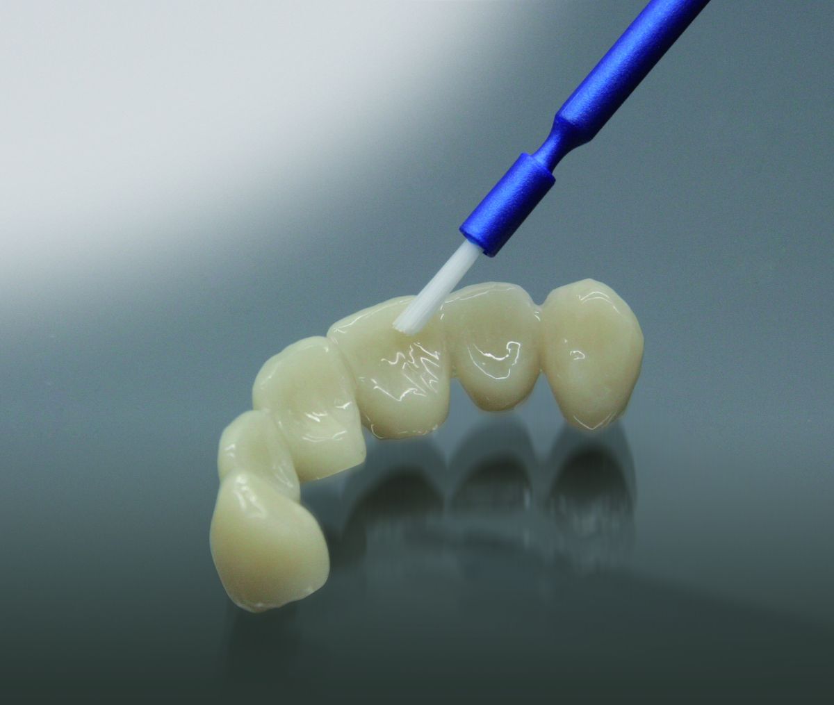 Lichthärtender Tempofit finish Lack auf provisorischen Zahnkronen mit blauem Applikator.