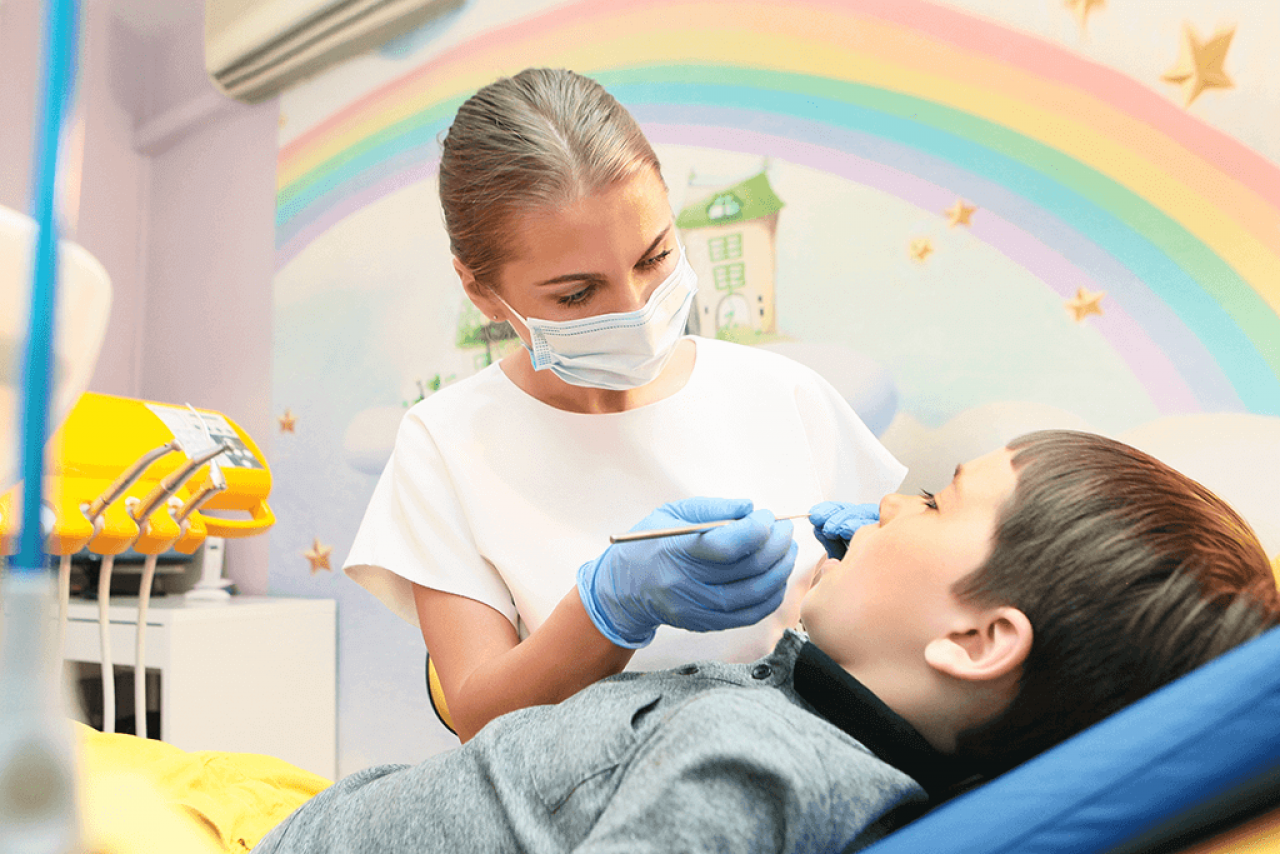 Zahnärztin mit Viawant Yellow Star Nitrilhandschuhen behandelt Kind unter Regenbogenmotiv.