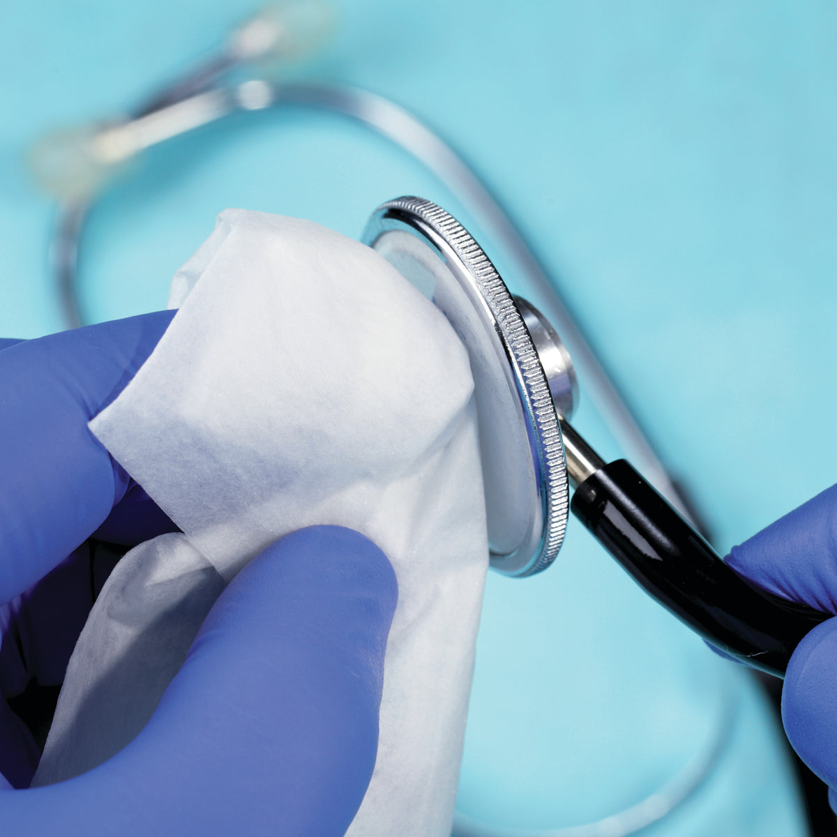 Nahaufnahme einer Hand in blauen Handschuhen, die ein Stethoskop mit Bacillol Desinfektionstuch reinigt.