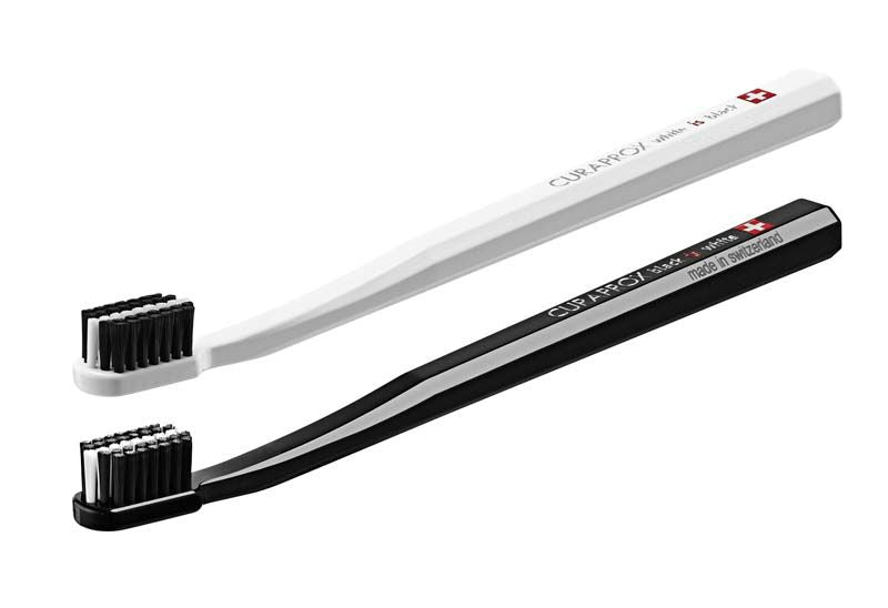 Zwei CURAPROX Black is White Zahnbürsten, eine schwarz, eine weiß, freigestellt.