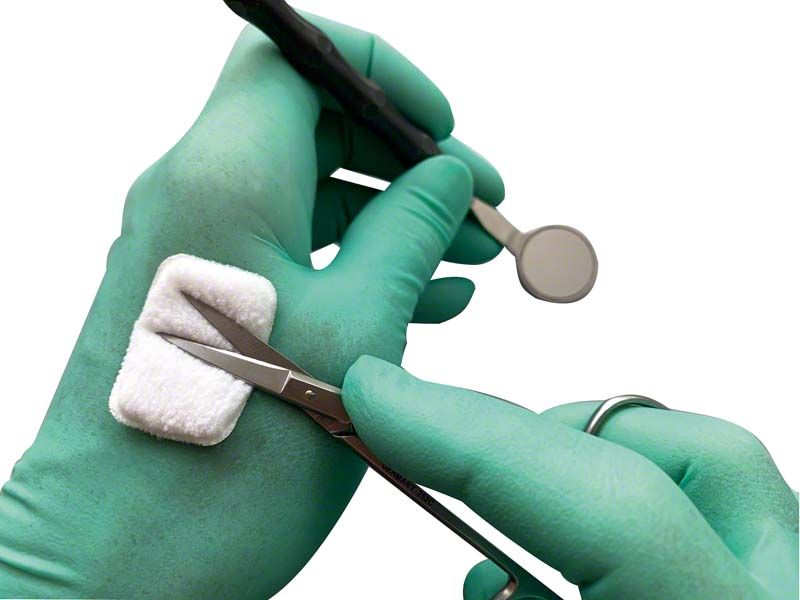 Selbstklebendes Reinigungspad auf grünem Handschuh mit Dentalinstrumenten.