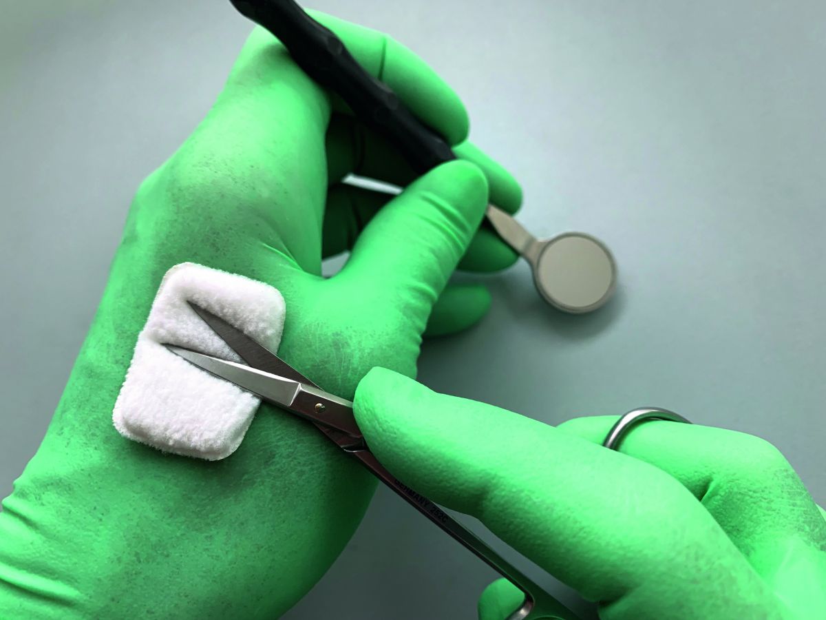 Selbstklebendes Reinigungspad auf grünem Handschuh mit Dentalinstrumenten im Einsatz.