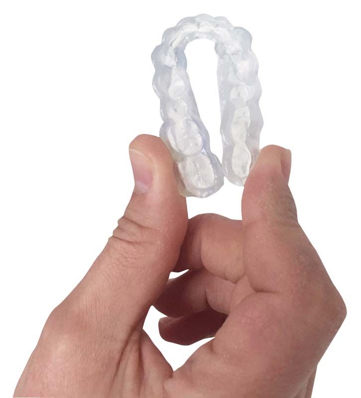 Detailansicht einer transparenten, flexiblen Zahnschiene in Hand gehalten.