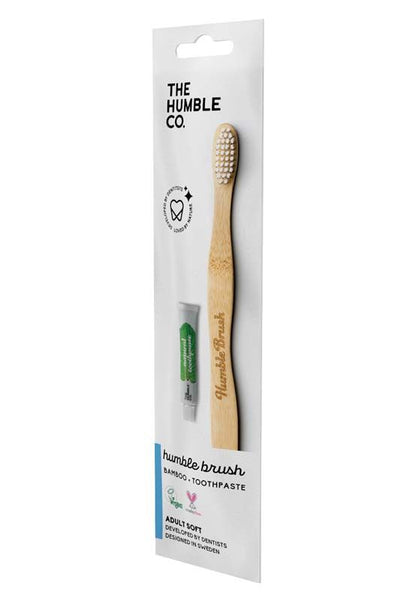 Bambuszahnbürste mit weichen Borsten und Zahnpastatube in geöffneter Verpackung.
