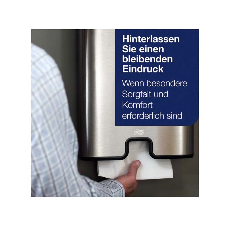 Person entnimmt Tork Multifold Handtuch aus Edelstahlspender mit blauem Hinweistext.