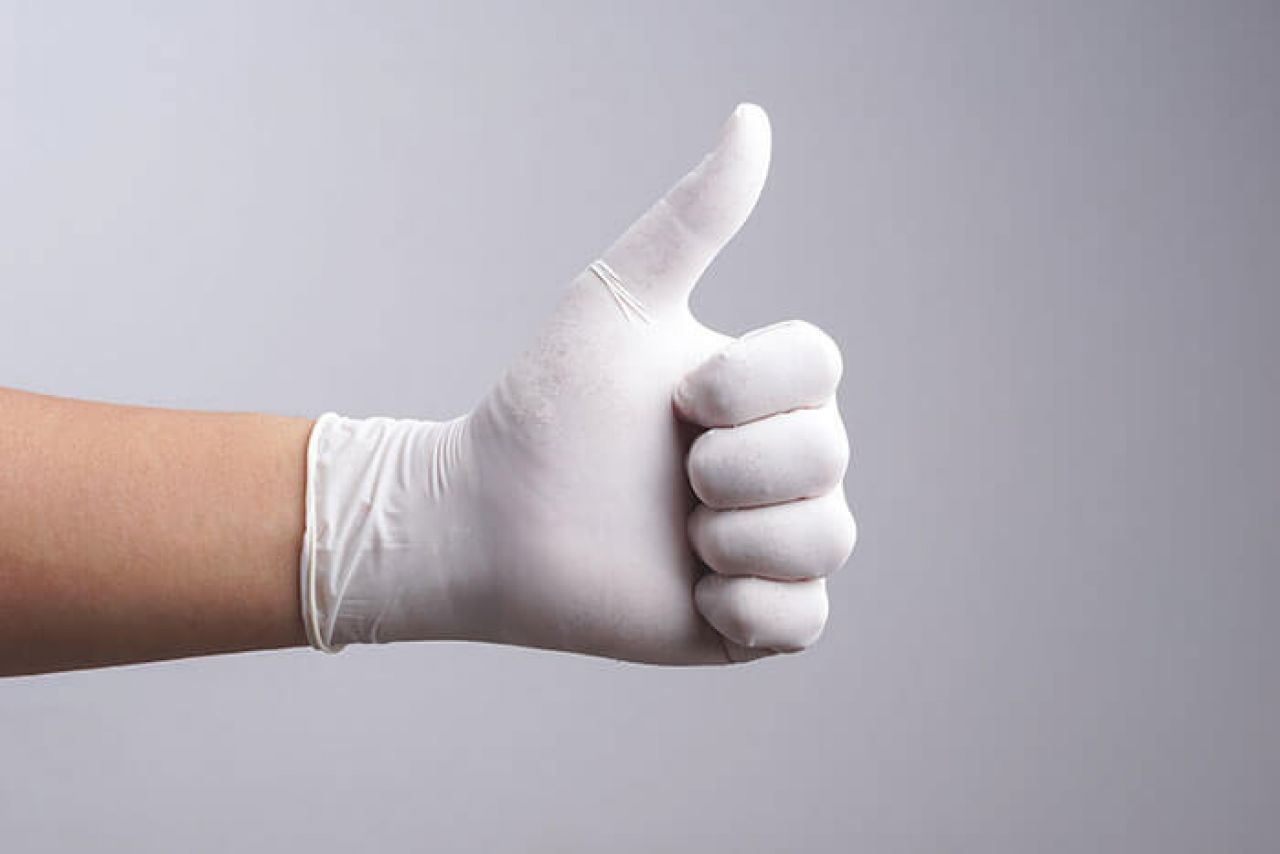 Weißer Nitrilhandschuh mit Daumen nach oben Geste.