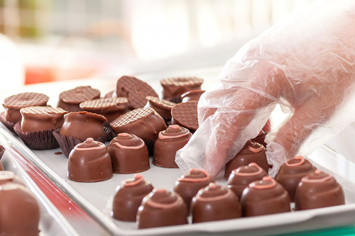Vinylhandschuh greift nach Praline in einer Süßwarenproduktion.
