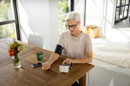 Ältere Frau misst Blutdruck mit Omron M400 Intelli IT, Smartphone daneben.