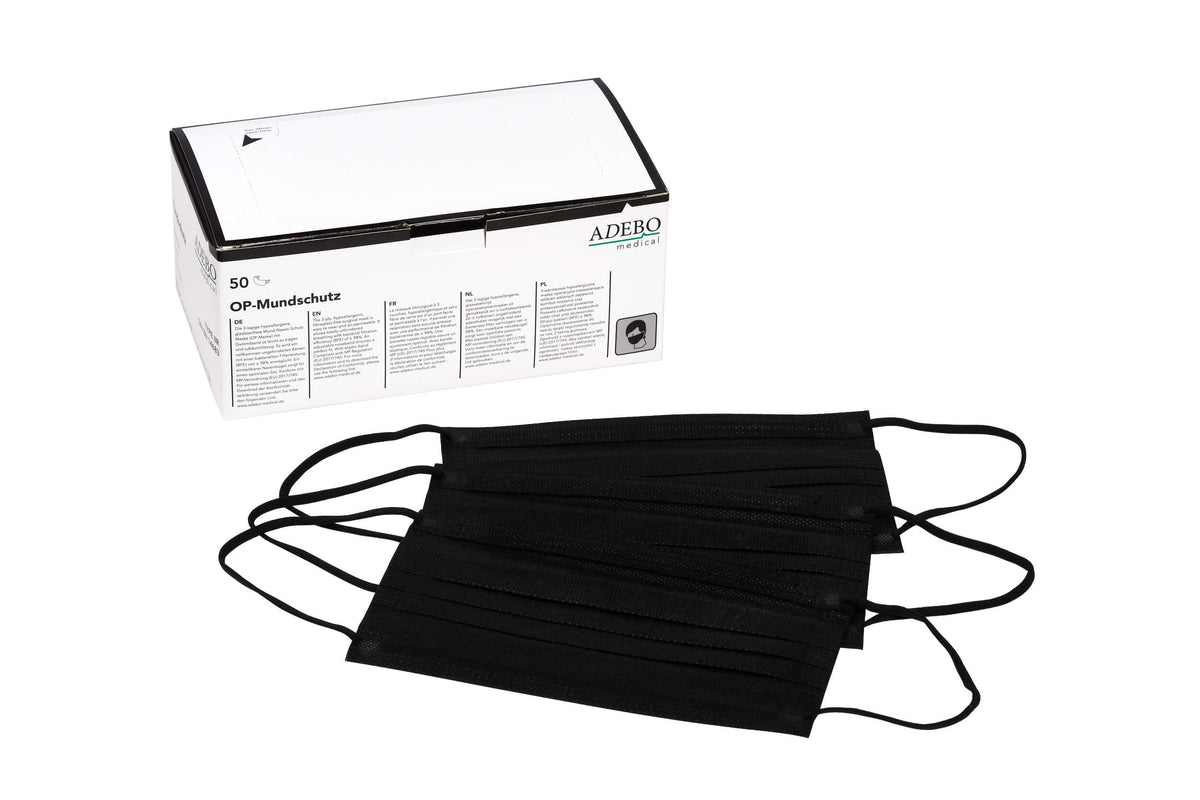 Schwarzer dreilagiger Mundschutz mit elastischen Bändern neben Verpackung.